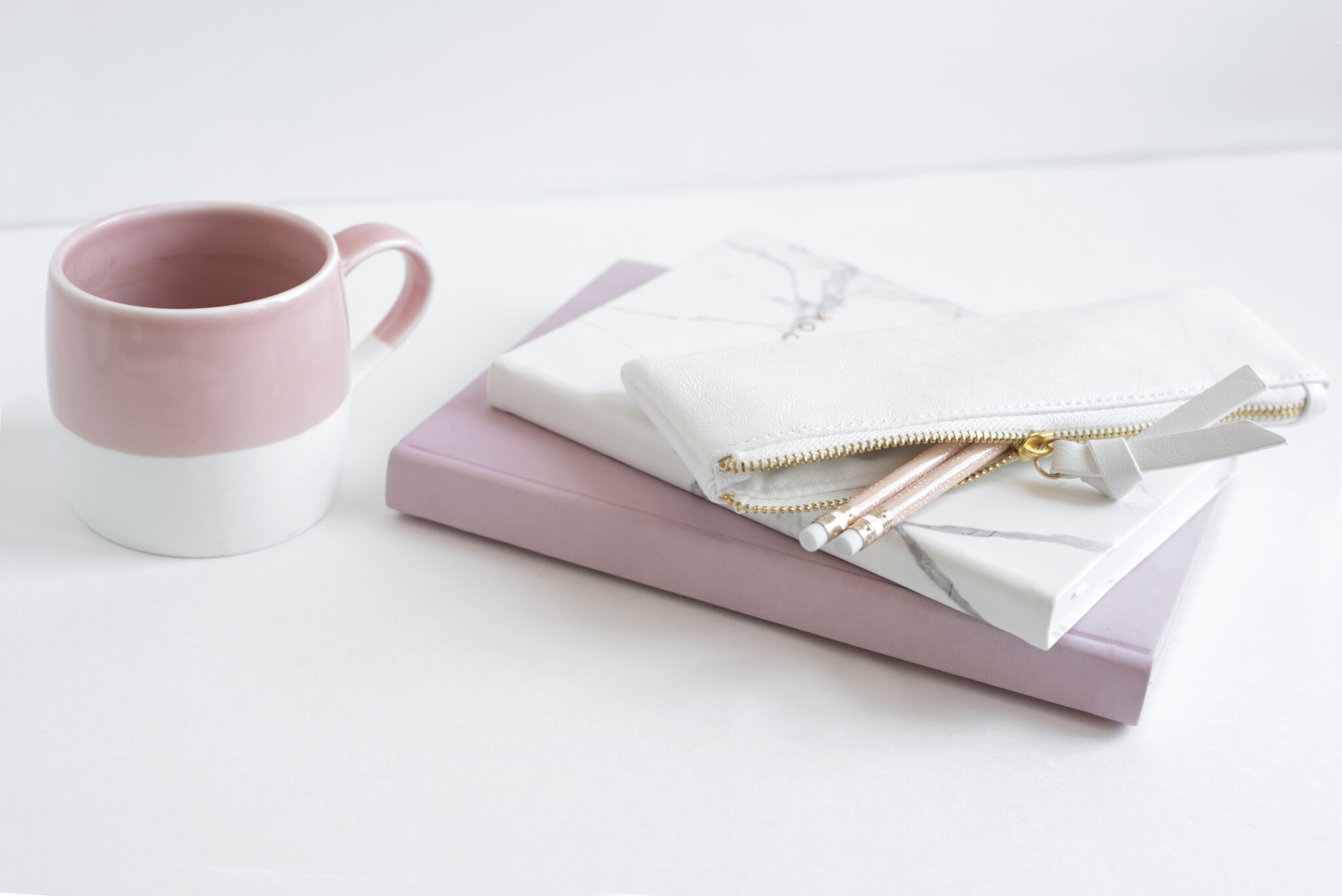 pink mug, pink notebook, and marble journal with pencil case on a marble desktop